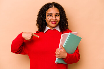 Young student African American woman isolated on beige background person pointing by hand to a shirt copy space, proud and confident