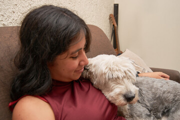 Portrait of Young latina woman hugging her bobtail dog on sofa.