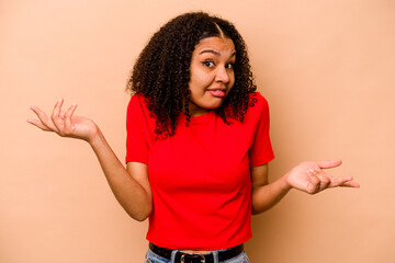 Young African American woman isolated on beige background doubting and shrugging shoulders in...