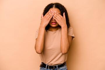 Young African American woman isolated on beige background afraid covering eyes with hands.
