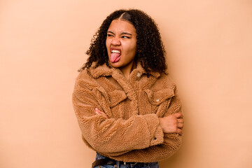 Young African American woman isolated on beige background funny and friendly sticking out tongue.