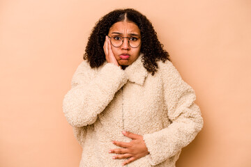 Young African American woman isolated on beige background blows cheeks, has tired expression....