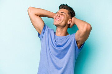 Young caucasian man isolated on blue background feeling confident, with hands behind the head.