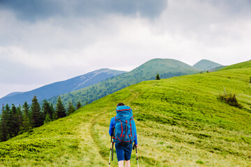 Obraz premium young man with backpack and trekking poles hiking in the mountains