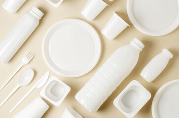 Disposable white plastic tableware on a beige background. The concept of nature pollution
