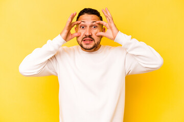 Fototapeta na wymiar Young hispanic man isolated on yellow background keeping eyes opened to find a success opportunity.