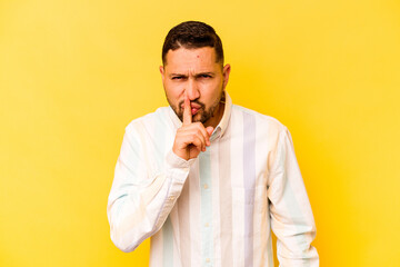 Young hispanic man isolated on yellow background keeping a secret or asking for silence.