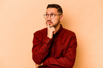 Fototapeta premium Young hispanic man isolated on beige background contemplating, planning a strategy, thinking about the way of a business.
