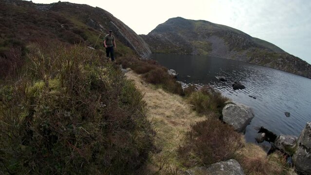 A man walking down to a mountain lake reservoir in Wales