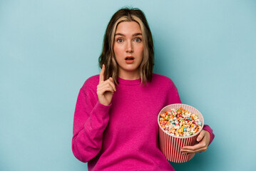 Young caucasian woman holding popcorn isolated on blue background having an idea, inspiration concept.