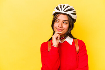 Young student hispanic woman wearing a bike helmet isolated on yellow background looking sideways with doubtful and skeptical expression.