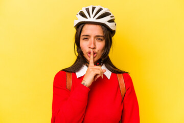 Young student hispanic woman wearing a bike helmet isolated on yellow background keeping a secret or asking for silence.