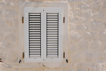 Fototapeta premium window with closed shutters on old white stone wall, renovation, reconstruction architecture, adriatic vintage travel card. closed possibilities concept. textured background