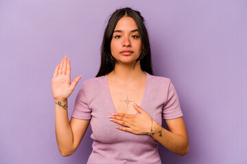 Obraz premium Young hispanic woman isolated on purple background taking an oath, putting hand on chest.