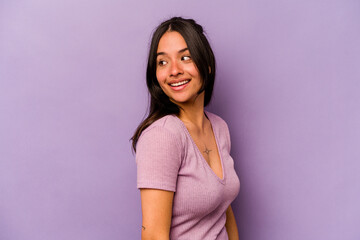 Young hispanic woman isolated on purple background looks aside smiling, cheerful and pleasant.