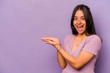Young hispanic woman isolated on purple background holding a copy space on a palm.