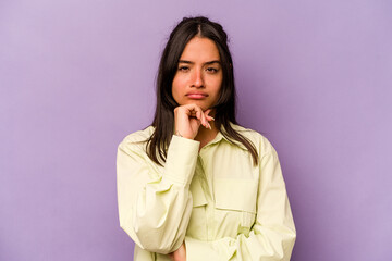 Young hispanic woman isolated on purple background suspicious, uncertain, examining you.