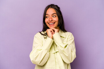 Young hispanic woman isolated on purple background keeps hands under chin, is looking happily aside.