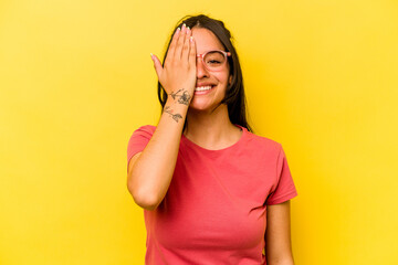 Young hispanic woman isolated on yellow background having fun covering half of face with palm.