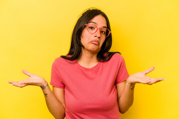 Young hispanic woman isolated on yellow background doubting and shrugging shoulders in questioning...
