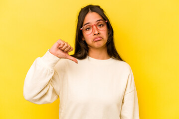 Young hispanic woman isolated on yellow background showing a dislike gesture, thumbs down....