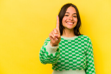 Young hispanic woman isolated on yellow background showing number one with finger.