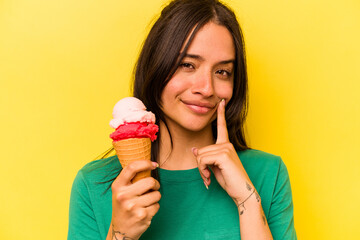 Young hispanic woman eating an ice cream isolated on yellow background
