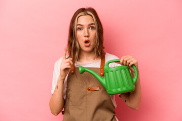 Young gardener woman holding watering can isolated on pink background having some great idea, concept of creativity. © Asier