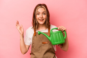 Young gardener woman holding watering can isolated on pink background receiving a pleasant surprise, excited and raising hands.