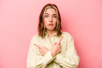 Young caucasian woman isolated on pink background points sideways, is trying to choose between two options.