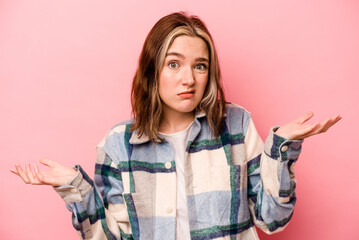 Young caucasian woman isolated on pink background doubting and shrugging shoulders in questioning...