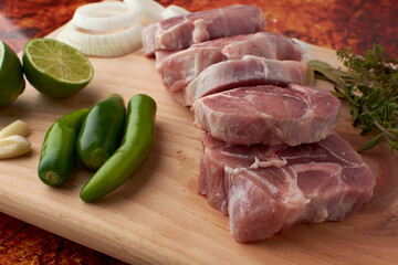Pork for tacos, knuckle, around there are serrano peppers, garlic, onion, oregano, thyme and bay leaves, lemon, placed on a wooden base.