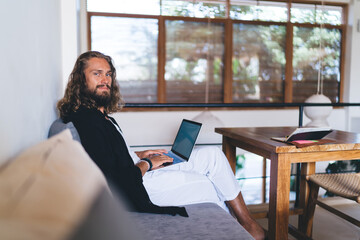 Portrait of long haired hipster guy posing with laptop device during remote working, Caucasian male...