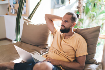 Pondering male IT software developer thoughtful looking away during remote working on laptop technology, skilled blogger with modern netbook thinking about content planning and graphic design
