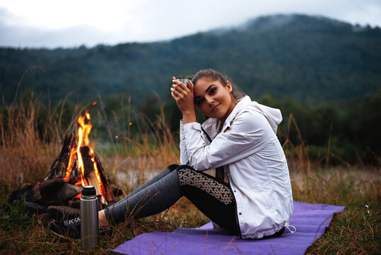 Female tourist drinking tea and sitting near bonfire