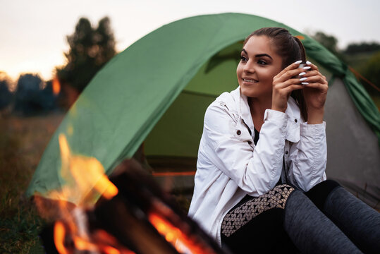 Woman drinking tea outdoors near tent and fire