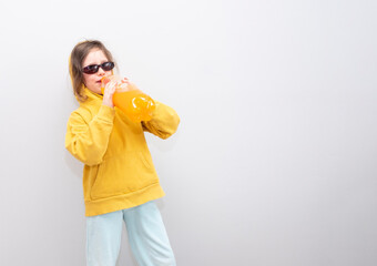 Child, Caucasian 6 years old, in a yellow sweatshirt with a hood on a gray background. The child rejoices and gesture holds a bottle of lemonade in his hands.