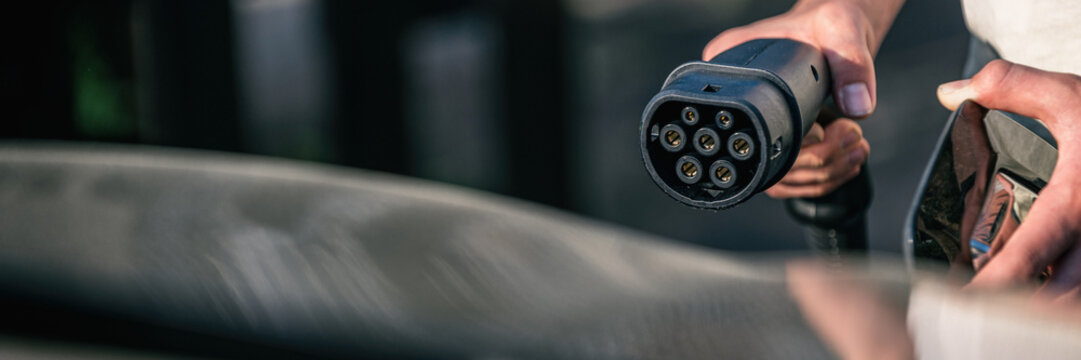 Hand h&auml;lt Ladekabel das an Elektroauto angeschlossen wird