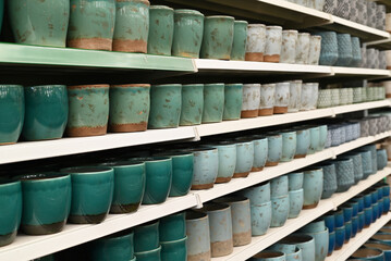 Fototapeta premium Rows of ceramic cups on display in a store, showcasing various shades of blue and green pottery.