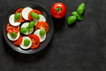 Caprese, Italian antipasto, mozzarella, tomato and basil on dark background, top view, space to copy text.