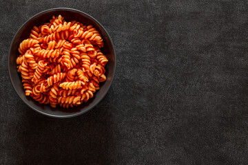 Fusilli, cooked pasta with tomato sauce, on dark background, top view, space to copy text.
