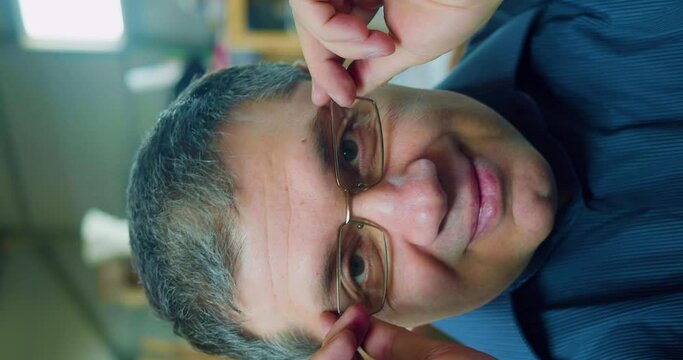 Portrait of a benevolent 50-year-old man. He puts on his glasses, smiles discreetly and looks into the camera.