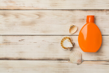 Bottle with sun protection cream and sea shells on wooden background, top view