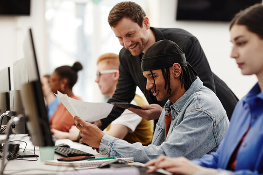 Side View Portrait Of Male Teacher Helping African American Student Using Computer In College Classroom, Copy Space