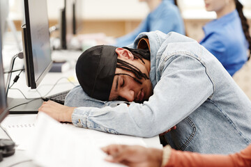 Vibrant portrait of young black student sleeping on desk in college classroom cramming for exams