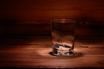 Empty shot glass on a wooden table. On a wooden background, close-up