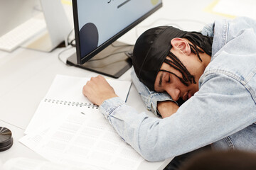 Minimal high angle portrait of young black student sleeping on desk in college classroom by computer