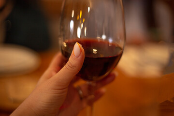 A woman hand is holding glass of red vine.