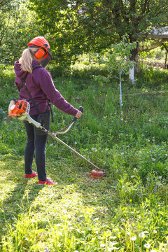 Woman farmer mows the grass in the backyard using string trimmer