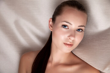 Beautiful Young Female Beauty Model with Fresh Makeup and Clean Hair with Studio Lighting against Beige Fabric. Nude Spa Beauty Concept